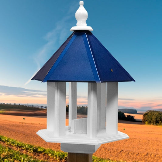 A white and navy blue bird feeder cap with a pointed white finial, shown outdoors against a blue sky and golden field background

perch & weather